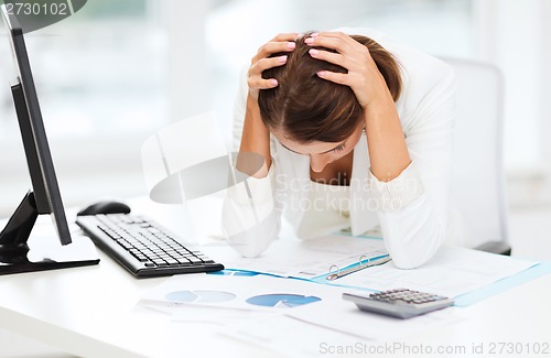 Image of stressed woman with computer, papers, calculator