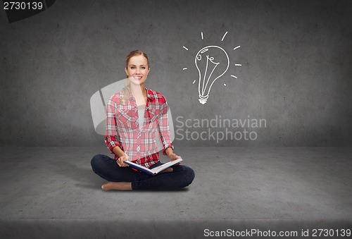 Image of smiling young woman sittin on floor with book