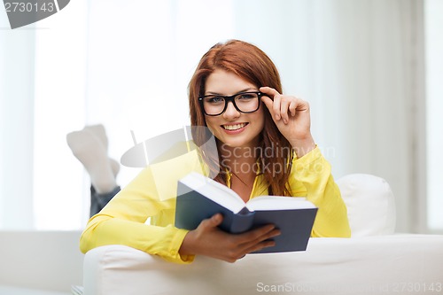 Image of smiling teenager reading book and sitting on couch