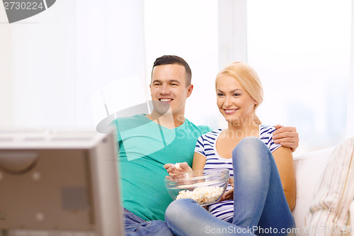 Image of smiling couple with popcorn watching movie at home