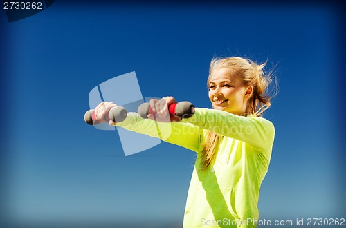 Image of sporty woman with light dumbbells outdoors