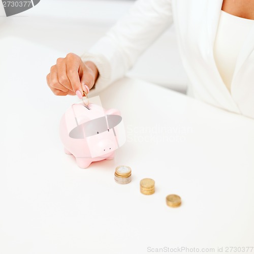 Image of female hand putting euro coins into piggy bank