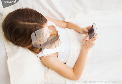 Image of little girl lying in bed with smartphone at home