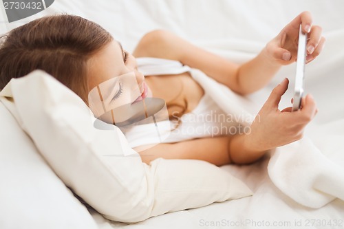 Image of little girl lying in bed with smartphone at home