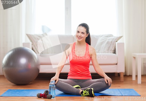 Image of smiling girl sitting on mat with sports equipment