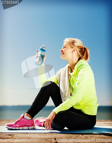 Image of woman drinking water after doing sports outdoors