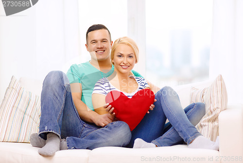 Image of smiling happy couple with red heart at home