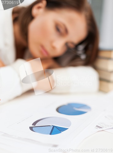 Image of bored businesswoman looking at graphs in office