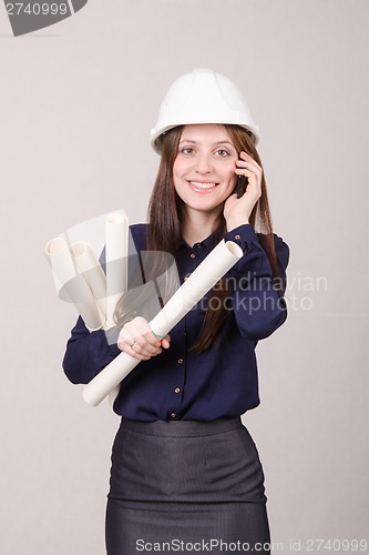 Image of Girl a helmet talking on phone with blueprints in hand