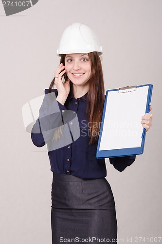 Image of Builder in helmet talking but phone with a folder hands