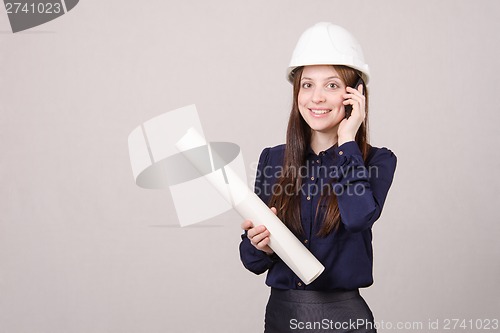 Image of Designer talking on phone with blueprints in hand