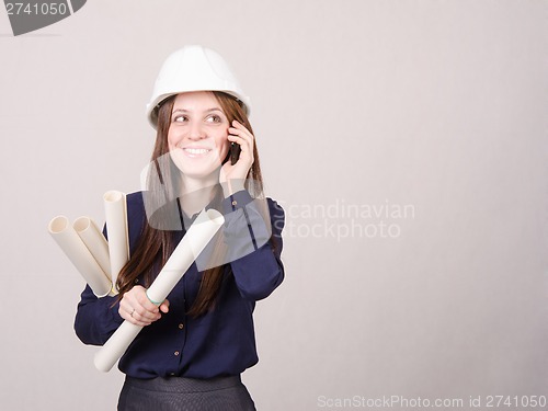 Image of Young woman talking on phone with blueprints in hand