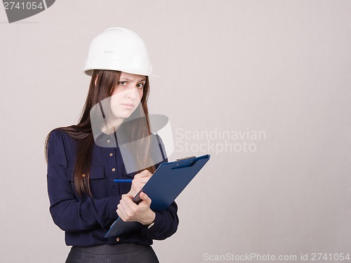 Image of Thoughtful girl a helmet writes in pencil folder