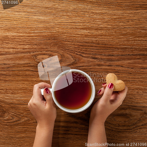 Image of woman holding hot cup of tea with cookies