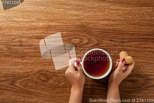 Image of woman holding hot cup of tea with cookies