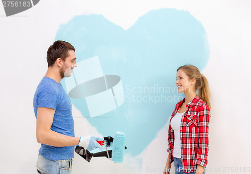 Image of smiling couple painting big heart on wall