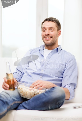 Image of smiling man with beer and popcorn at home