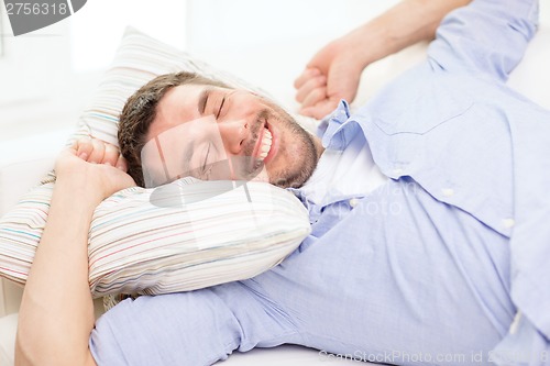 Image of smiling young man lying on sofa at home