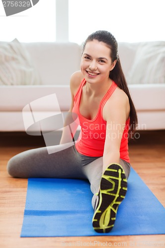 Image of smiling teenage girl streching on floor at home