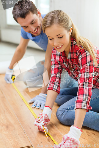 Image of smiling couple measuring wood flooring