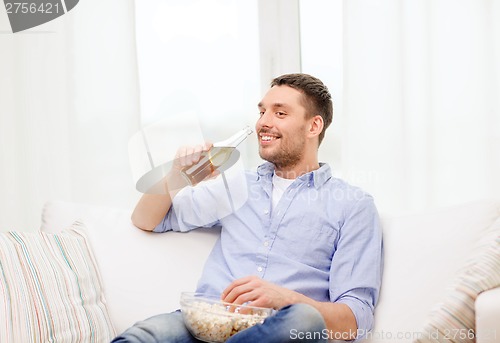 Image of smiling man with beer and popcorn at home