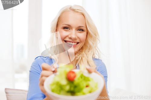 Image of smiling young woman with green salad at home