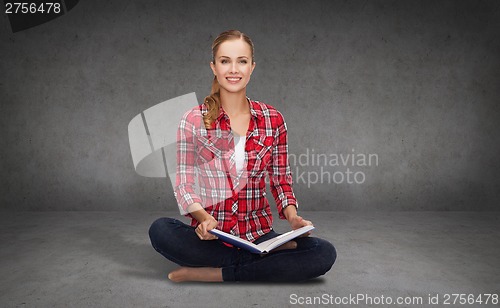 Image of smiling young woman sittin on floor with book