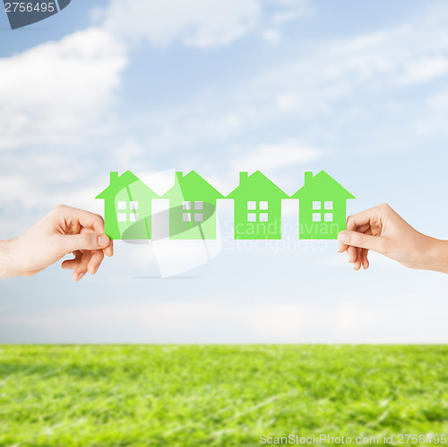 Image of man and woman hands with many green paper houses