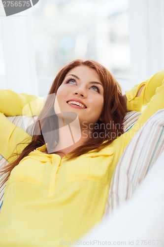 Image of smiling young woman lying on sofa at home