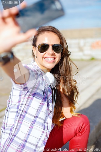 Image of smiling teenager taking picture with smartphone