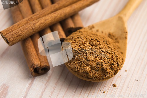 Image of Cinnamon, whole sticks behind wooden spoon with a heap of powder