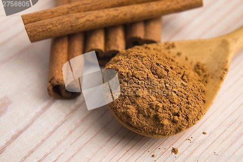 Image of Cinnamon, whole sticks behind wooden spoon with a heap of powder