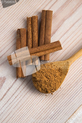 Image of Cinnamon, whole sticks behind wooden spoon with a heap of powder