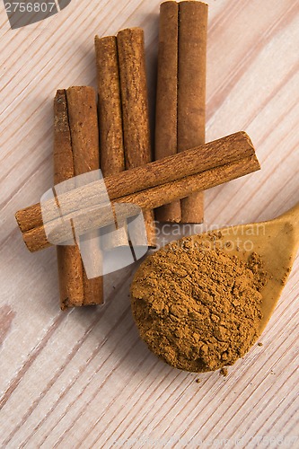 Image of Cinnamon, whole sticks behind wooden spoon with a heap of powder