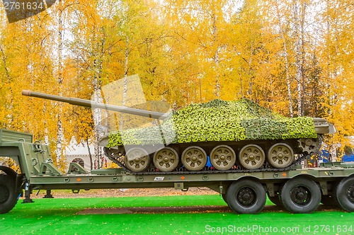 Image of Tank under camouflage network on truck platform