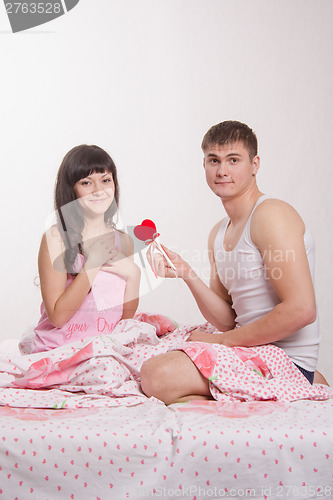 Image of Young man gives heart beautiful girl in bed