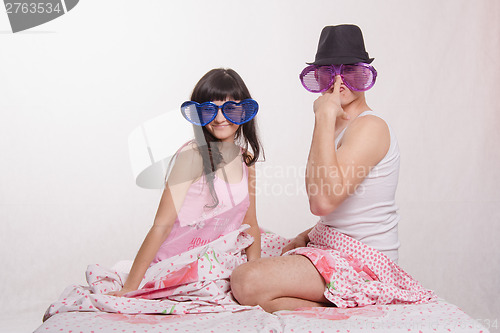 Image of Young couple sitting bed with big glasses, guy in hat