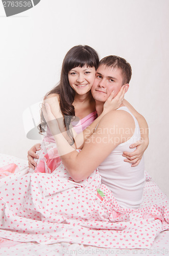 Image of Young couple embracing, sitting in bed