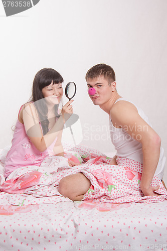 Image of Girl with magnifying glass considers clown nose Man