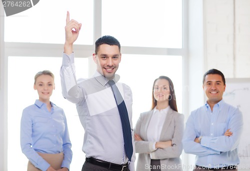 Image of smiling businessman in office with team on back