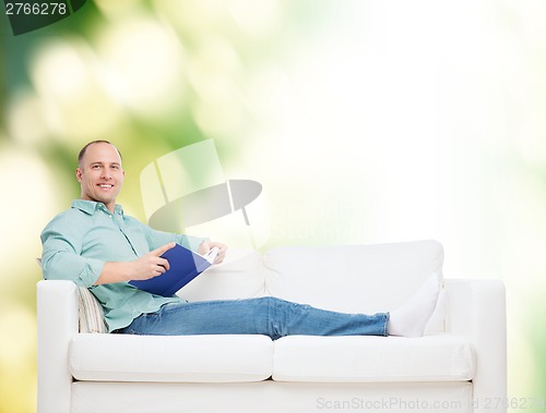 Image of smiling man lying on sofa with book