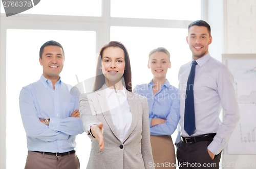 Image of smiling businesswoman in office with team on back