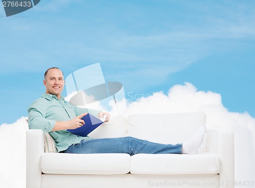 Image of smiling man lying on sofa with book