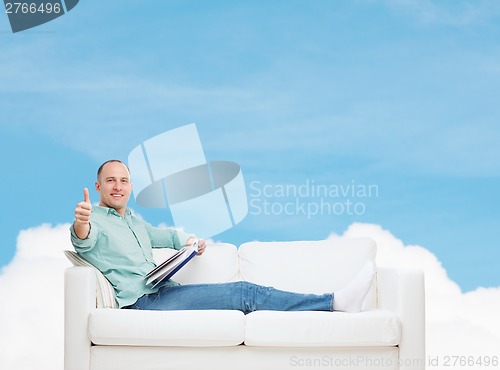 Image of smiling man lying on sofa with book