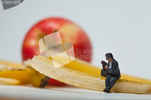 Image of Miniature people in action stting on a banan