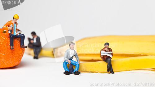 Image of Miniature people in action stting on a banan