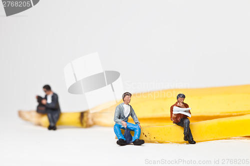 Image of Miniature people in action stting on a banan