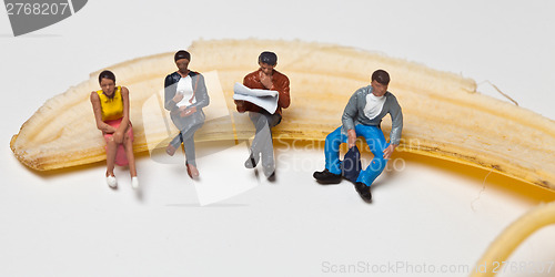 Image of Miniature people in action stting on a banan