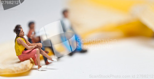 Image of Miniature people in action stting on a banan