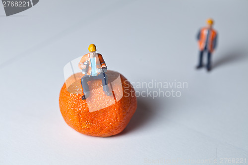 Image of Miniature people in action and man sitting on an orange